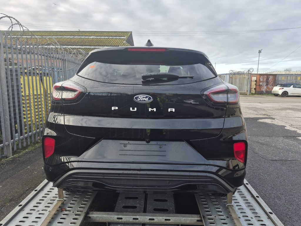 Rear of a new black Ford Puma Gen-E with PUMA lettering, loaded for EV transport to a Ford dealer